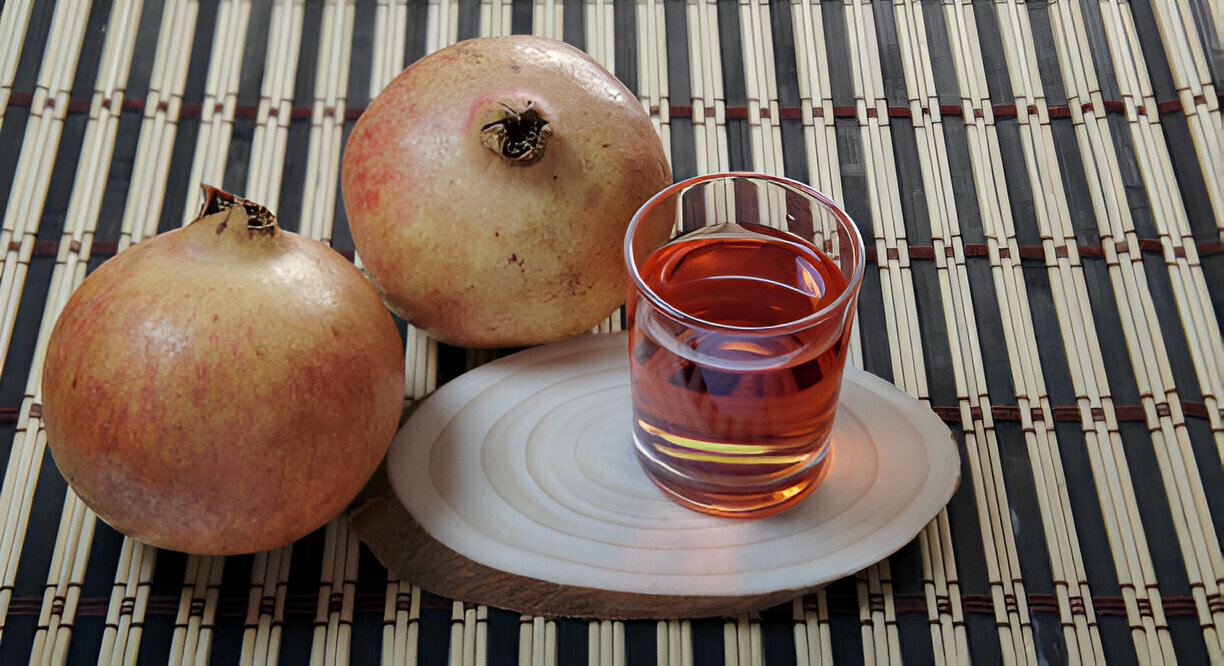 Duas romãs em cima da mesa e um copo de suco de romã do lado.